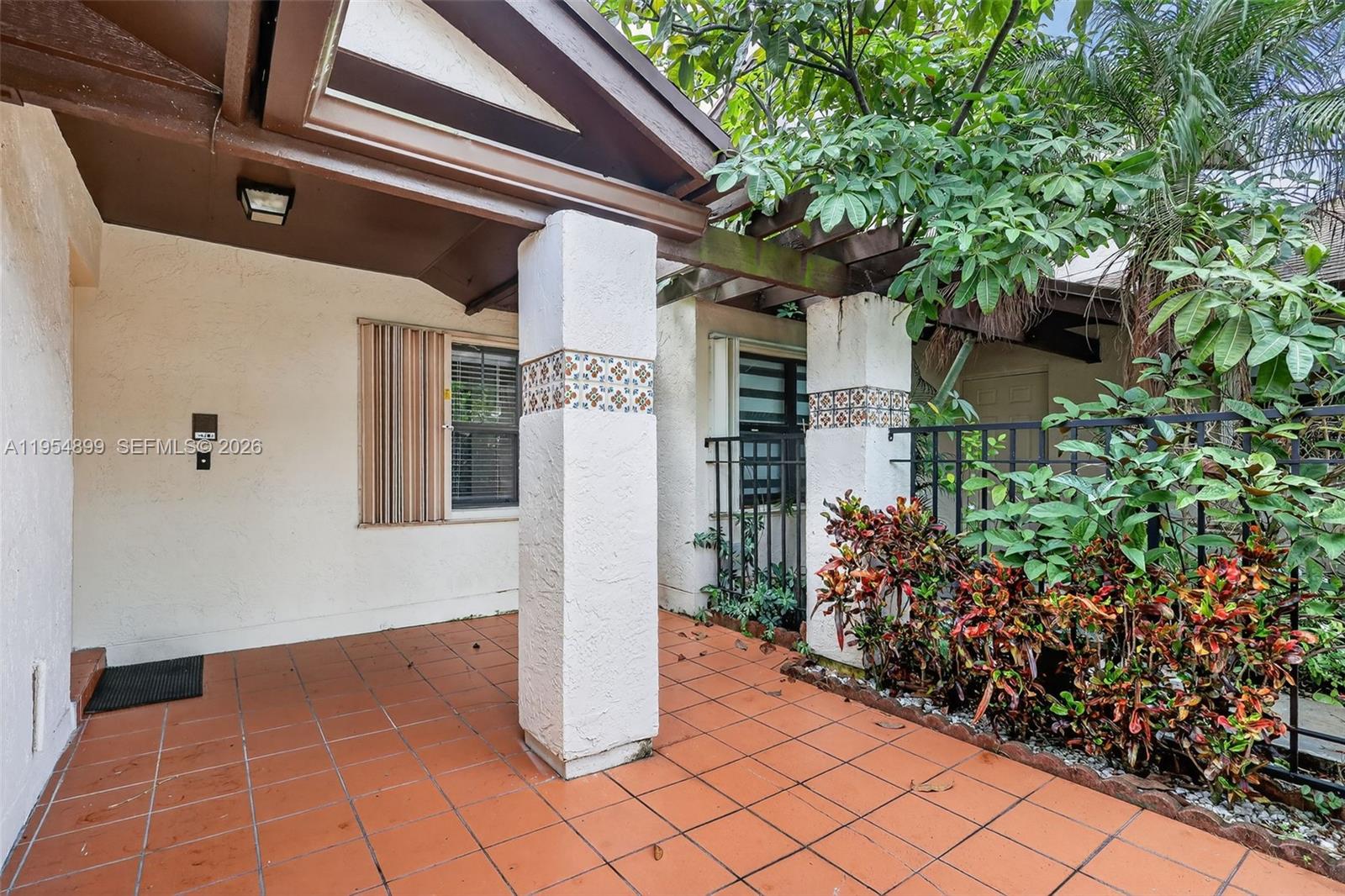A covered patio features terracotta tile flooring, two stucco columns with decorative tile accents, and landscaping — 13702 SW 101st Ter, Miami FL 33186, MIAMI, FL