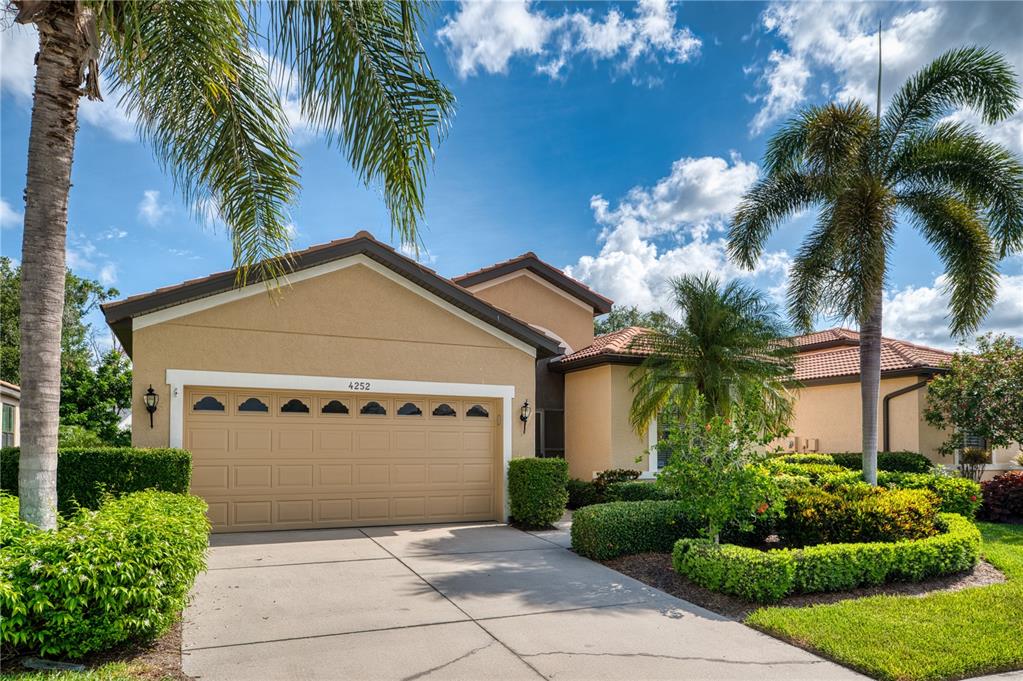 A tan stucco house with a two-car garage and palm trees under a blue sky — 4252 MACKAY FALLS TERRACE, SARASOTA, FL