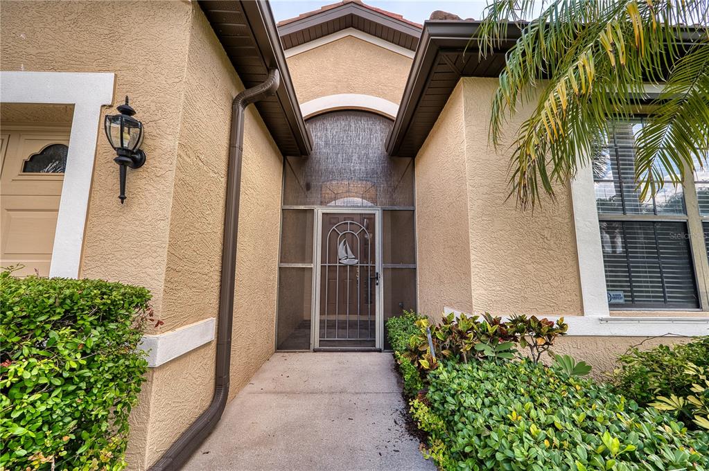 The exterior entrance features a screened-in front door with a sailboat design and stucco walls — 4252 MACKAY FALLS TERRACE, SARASOTA, FL