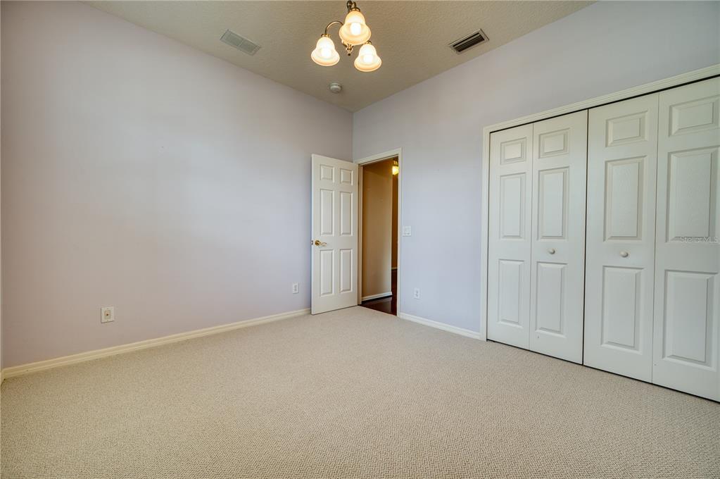 A bedroom with light purple walls, beige carpeting, a ceiling light fixture, and white closet doors — 4252 MACKAY FALLS TERRACE, SARASOTA, FL