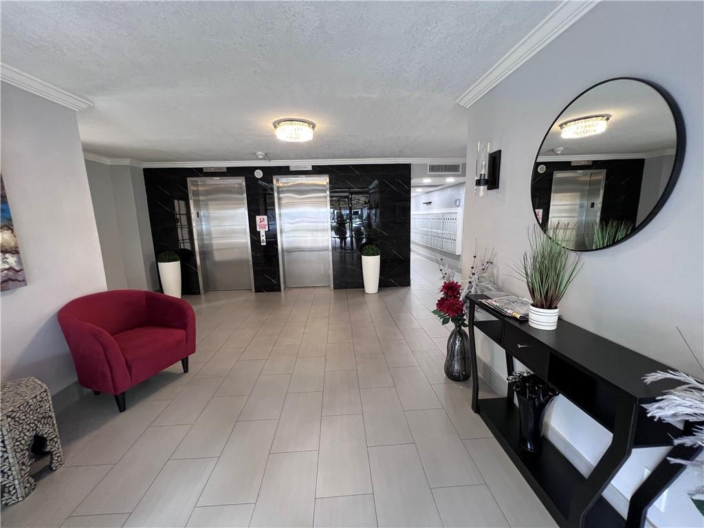 This apartment lobby features two elevators, a red armchair, a console table, and tile flooring — 3000 S Course Drive # 209, Pompano Beach FL 33069, POMPANO BEACH, FL