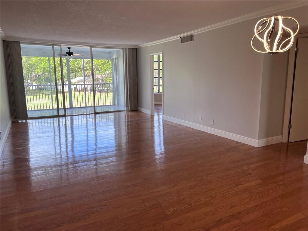 An empty living room features polished hardwood floors, a modern chandelier, and sliding glass doors — 3000 S Course Drive # 209, Pompano Beach FL 33069, POMPANO BEACH, FL