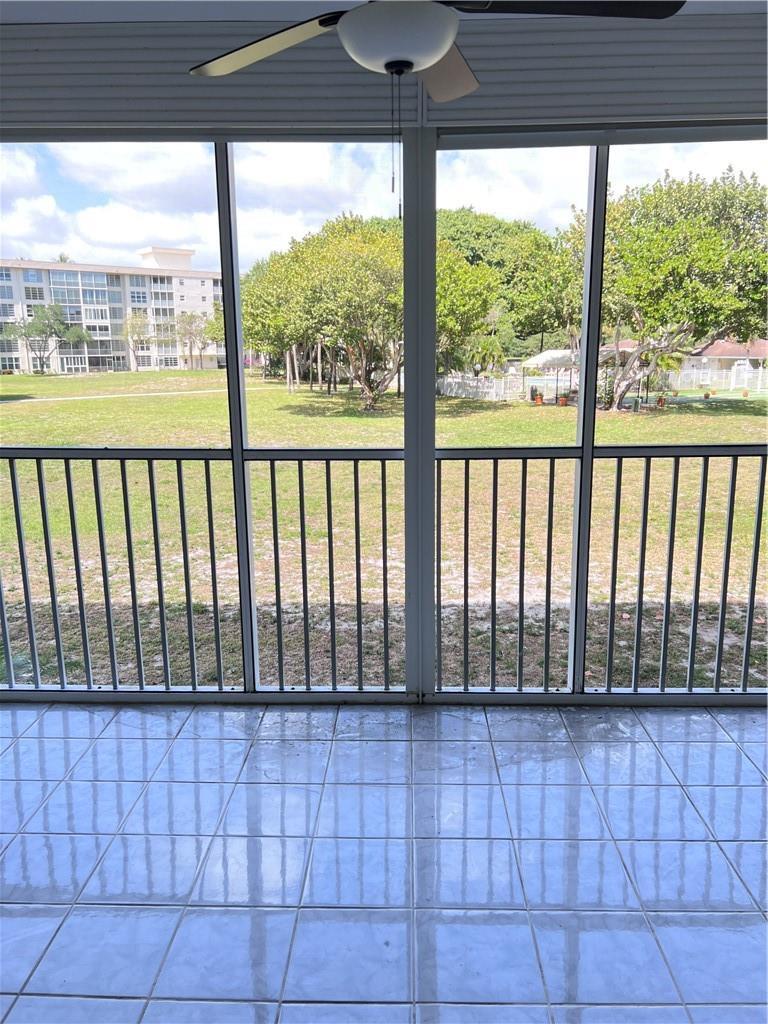 A tiled screened-in porch overlooks a grassy lawn and trees with a building in distance — 3000 S Course Drive # 209, Pompano Beach FL 33069, POMPANO BEACH, FL