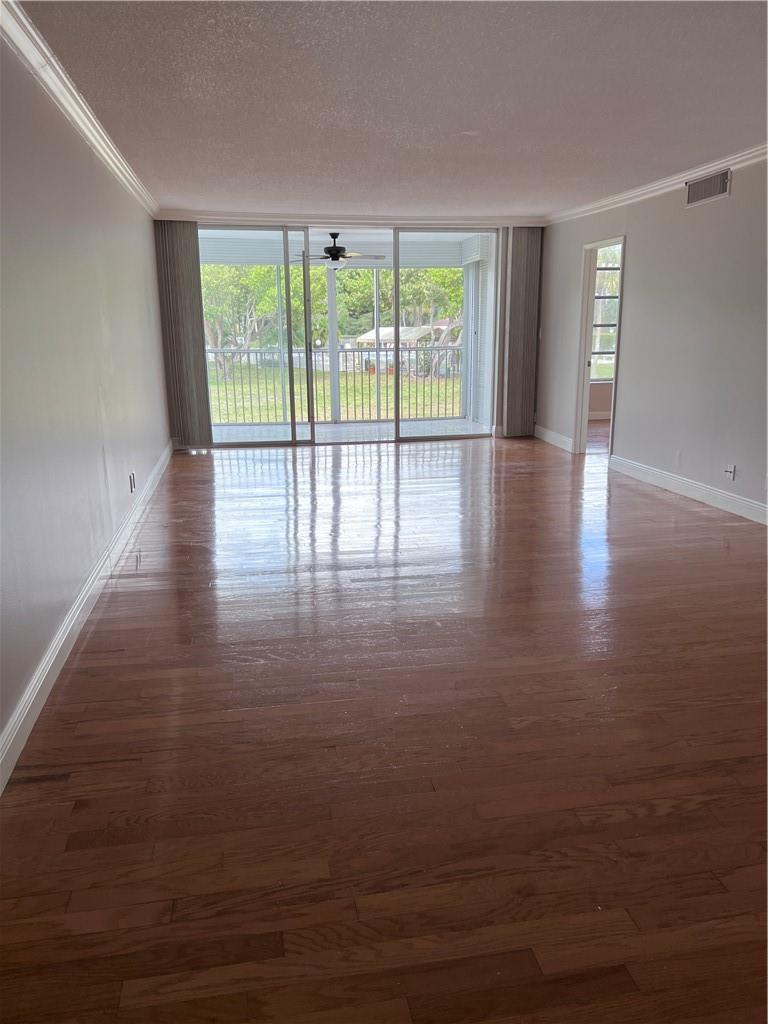 An empty living room features hardwood floors, light gray walls, and a sliding glass door — 3000 S Course Drive # 209, Pompano Beach FL 33069, POMPANO BEACH, FL