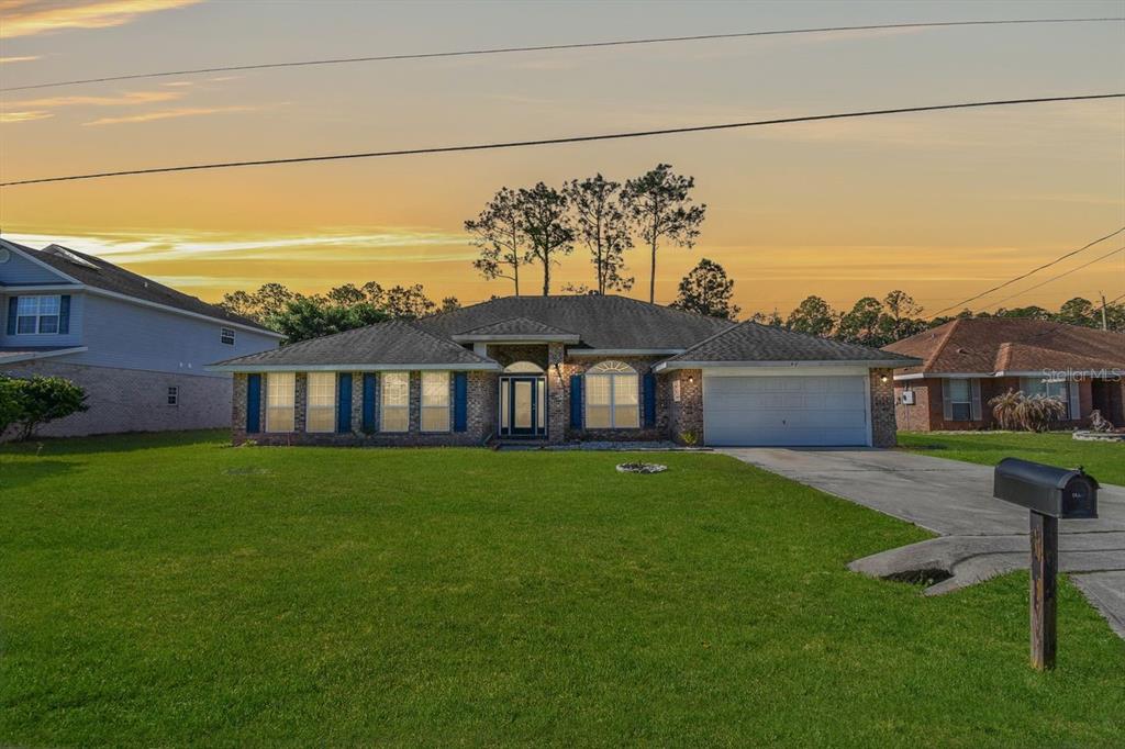 A single-story brick house with a two-car garage and a large front lawn at sunset — 46 RIDDLE DRIVE, PALM COAST, FL