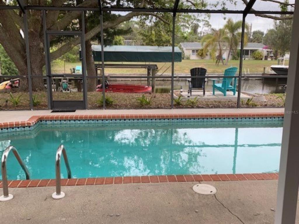 A swimming pool sits on a patio enclosed by a screen overlooking a canal — 18312 DRIGGERS AVENUE, PORT CHARLOTTE, FL