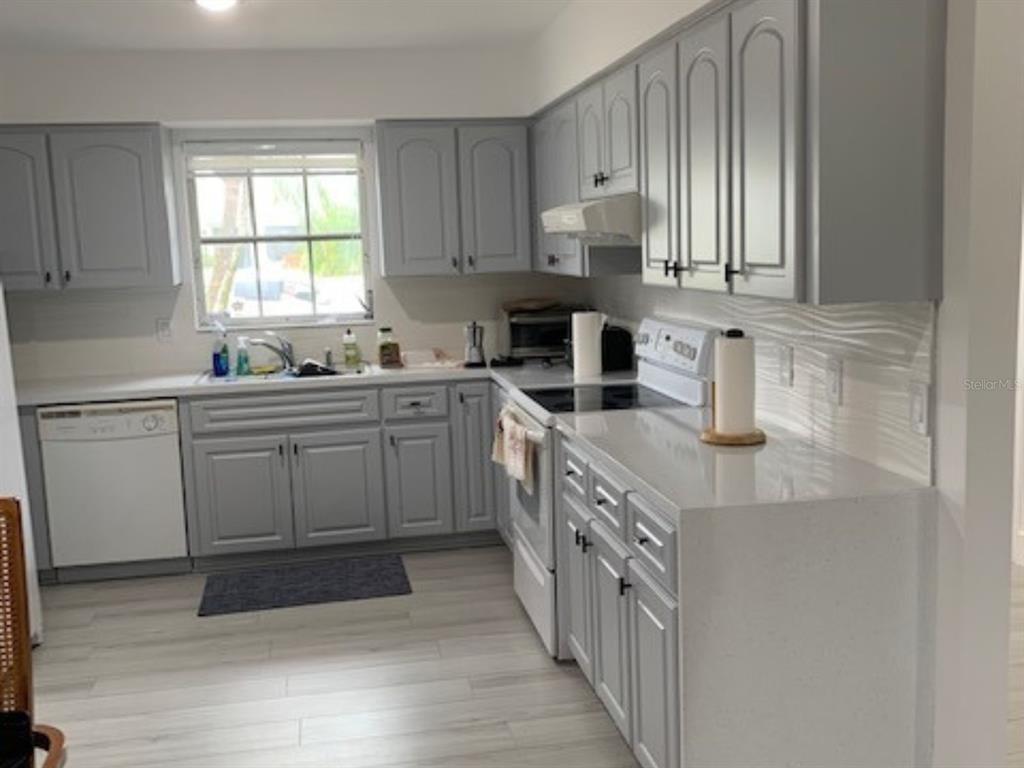 A kitchen with grey cabinets, white countertops, a white dishwasher, and light wood-look flooring — 18312 DRIGGERS AVENUE, PORT CHARLOTTE, FL