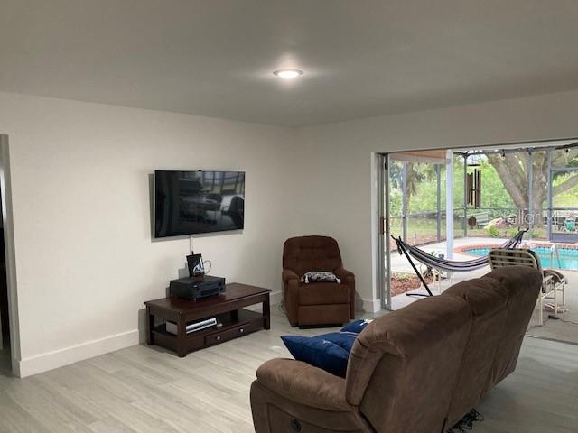 A living room features a wall-mounted television, brown furniture, and sliding doors opening to a pool — 18312 DRIGGERS AVENUE, PORT CHARLOTTE, FL