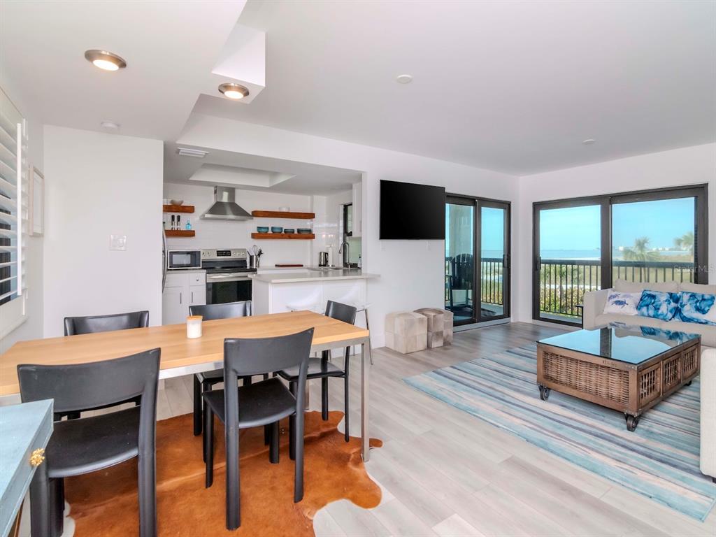 An open-concept living and dining area features a kitchen, wood-look flooring, and a beach view — 3200 GULF BOULEVARD UNIT 103, ST PETE BEACH, FL