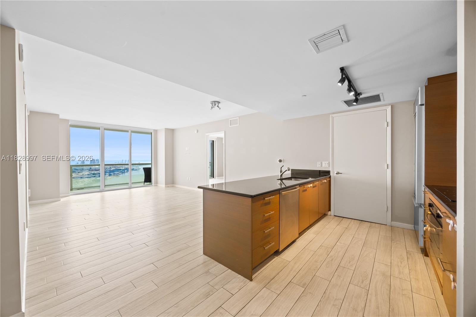 An open-concept kitchen with wood cabinets and dark countertops overlooks a living area with floor-to-ceiling windows — 50 Biscayne Blvd # 4706, Miami FL 33132, MIAMI, FL