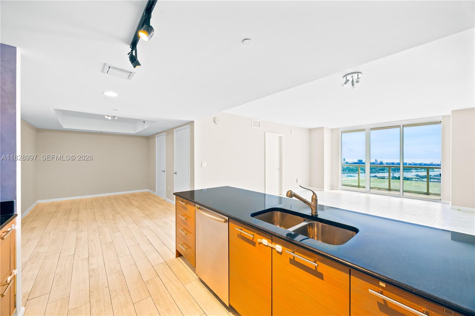 A kitchen island with a dark countertop and wood cabinets overlooks an open living area — 50 Biscayne Blvd # 4706, Miami FL 33132, MIAMI, FL