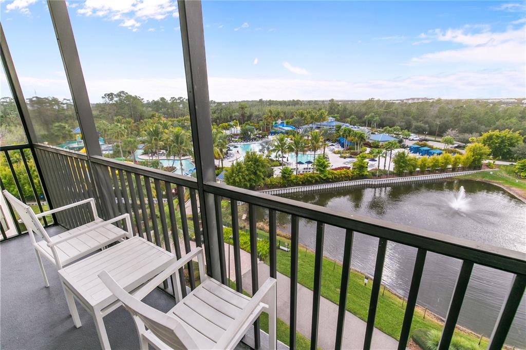 A balcony with two chairs overlooks a resort pool area and a pond with fountain — 14501 GROVE RESORT AVENUE UNIT 3619, WINTER GARDEN, FL