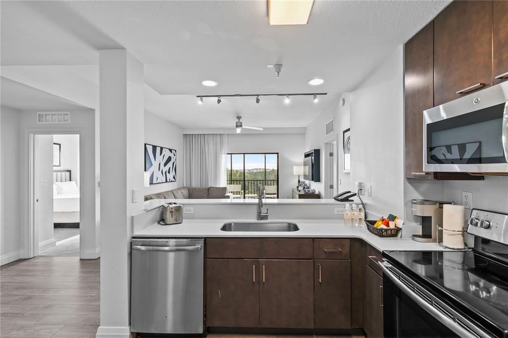 A kitchen with stainless steel appliances and dark cabinets overlooks a living area and balcony — 14501 GROVE RESORT AVENUE UNIT 3619, WINTER GARDEN, FL