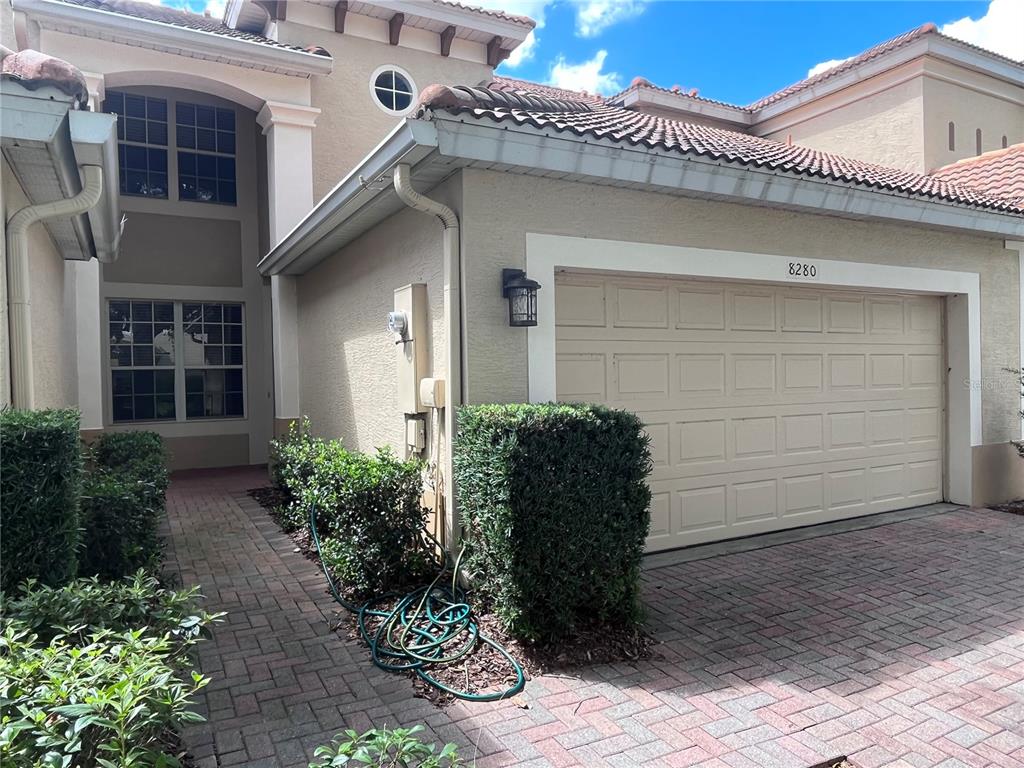 A beige two-story house features a tiled roof, a garage, and a brick paver driveway — 8280 VIA VIVALDI, ORLANDO, FL