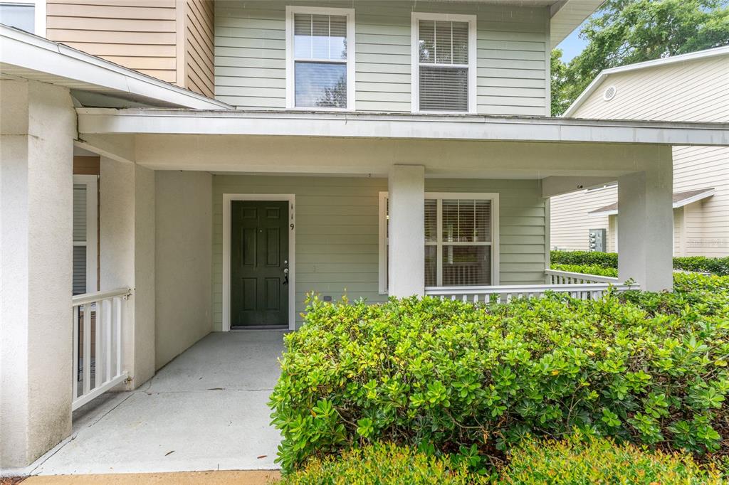 The exterior of a two-story house features a covered porch, green siding, and landscaping — 4680 SW 48TH WAY UNIT 119, GAINESVILLE, FL