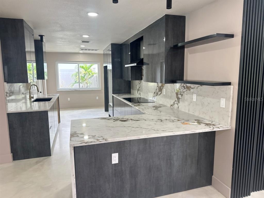 A modern kitchen features dark gray cabinetry, white marble countertops, and a matching marble backsplash — 3197 WALNUT STREET NE, ST PETERSBURG, FL