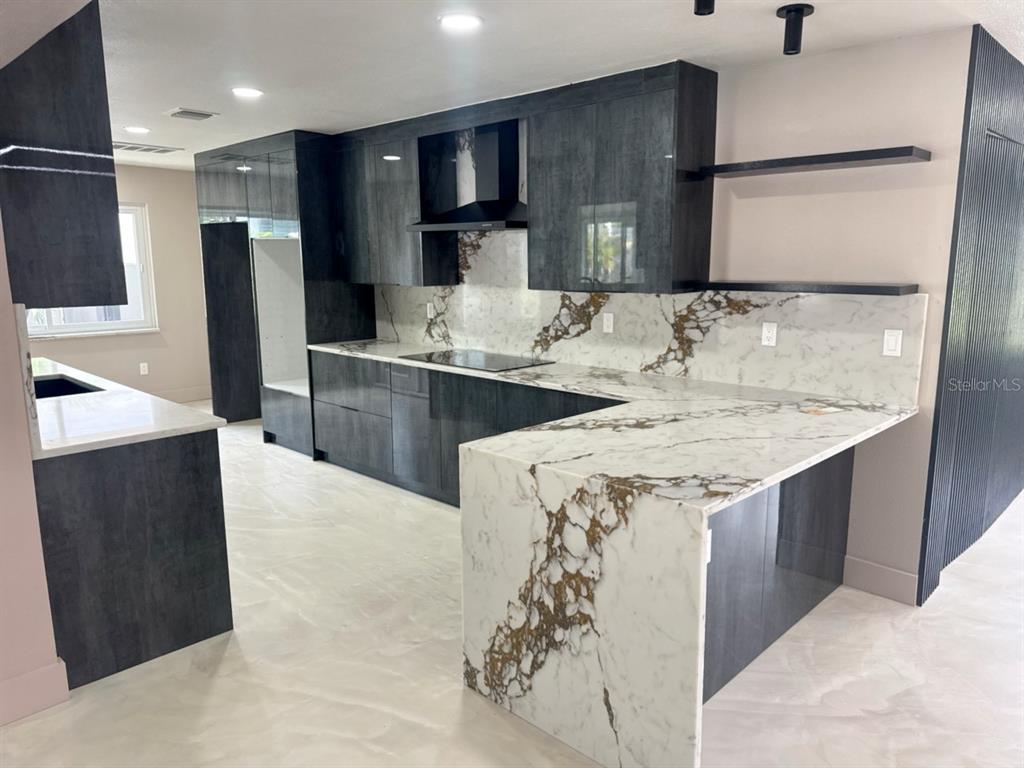 A modern kitchen features dark cabinetry, a waterfall marble island, and matching marble backsplash — 3197 WALNUT STREET NE, ST PETERSBURG, FL