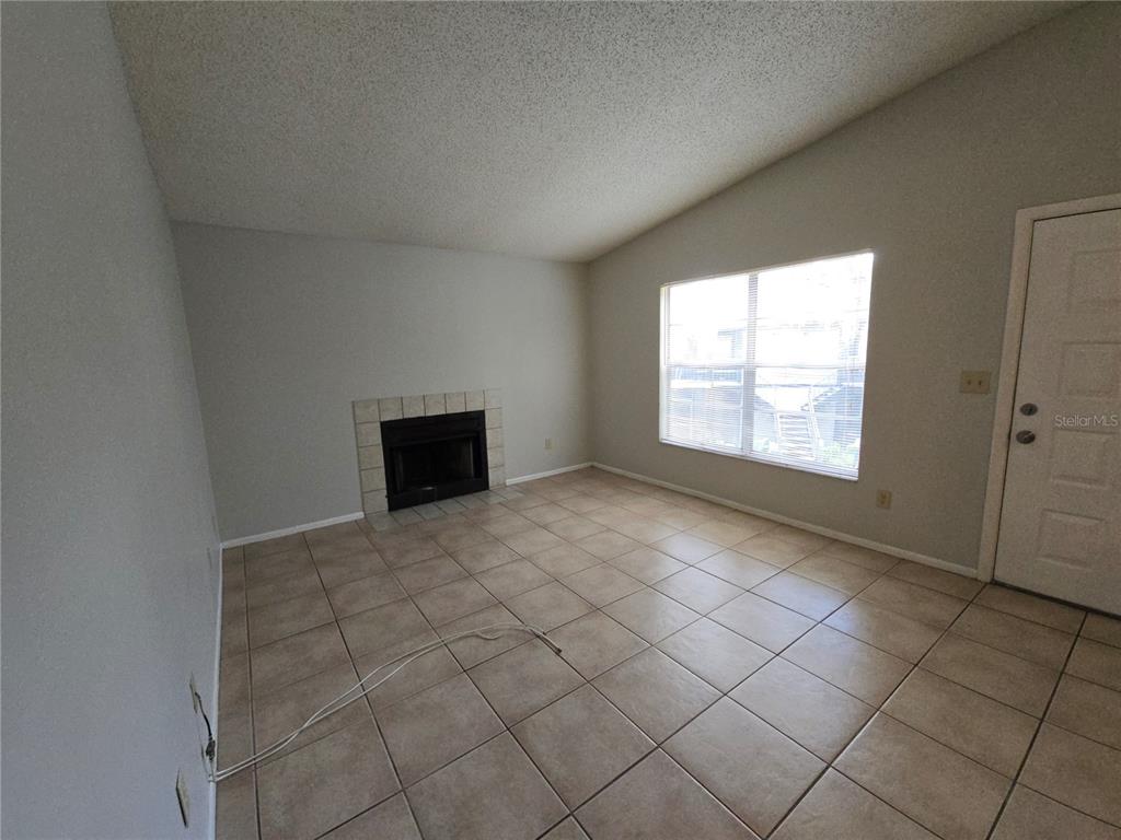 An empty living room features beige tile flooring, a fireplace, and a large window — 4031 TUMBLE WOOD TRAIL UNIT 203, TAMPA, FL