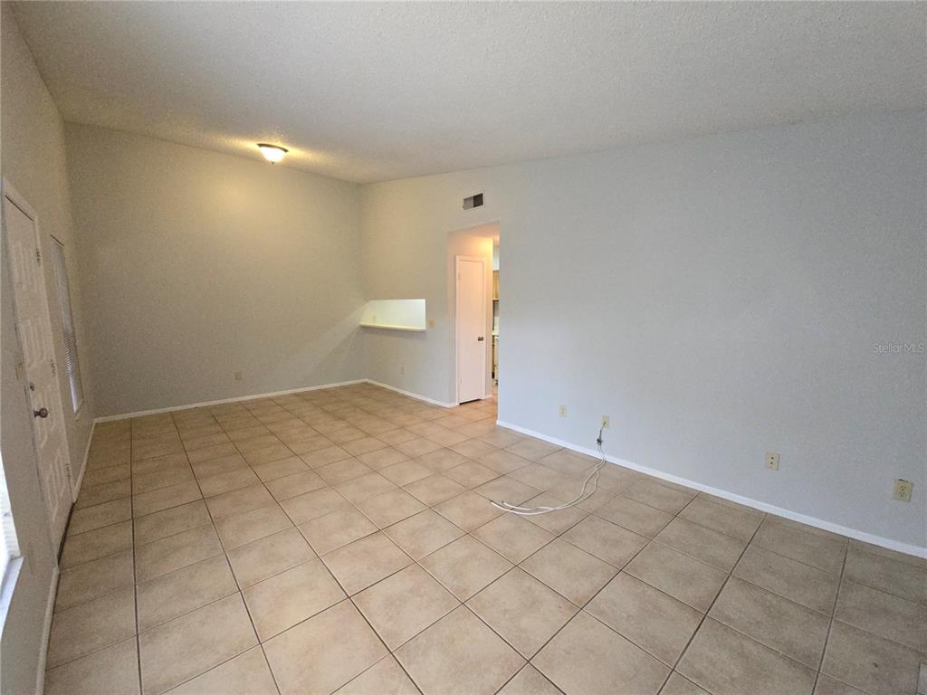 An empty living room features light-colored walls, beige tile flooring, and a small pass-through window — 4031 TUMBLE WOOD TRAIL UNIT 203, TAMPA, FL