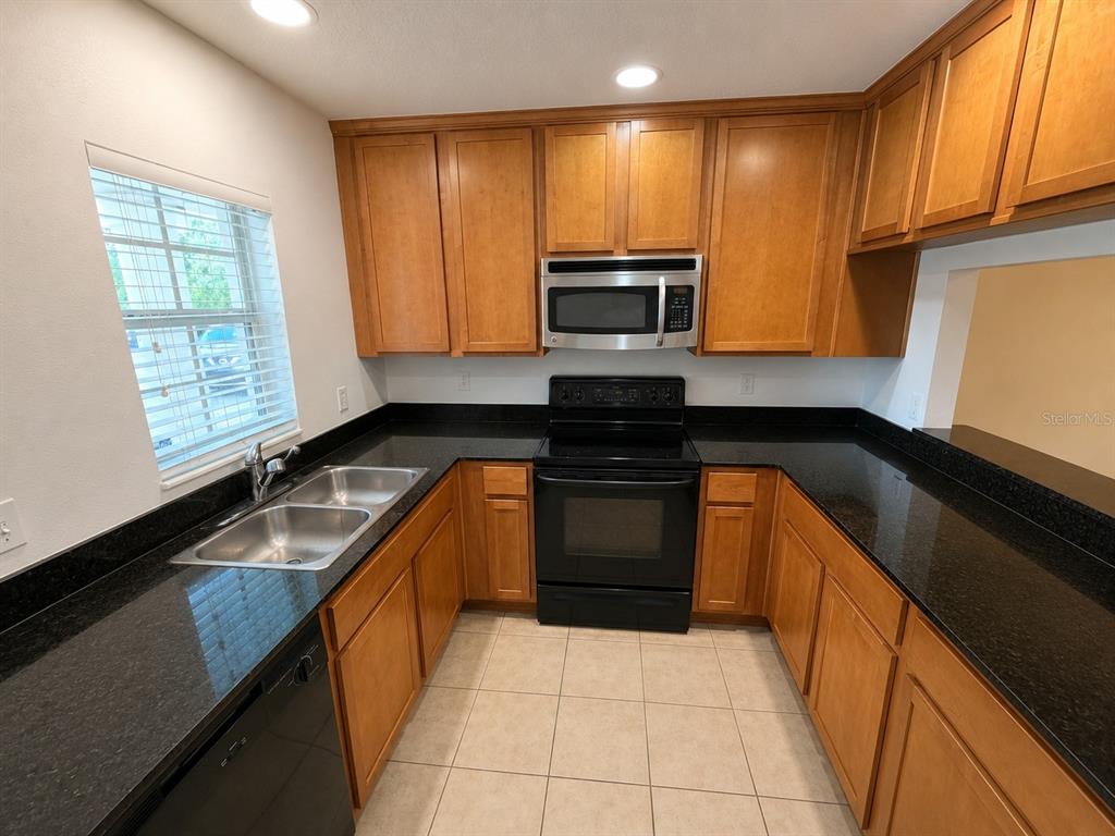 A kitchen features wood cabinets, black countertops, stainless steel appliances, and tile flooring — 9410 CHARLESBERG DRIVE, TAMPA, FL