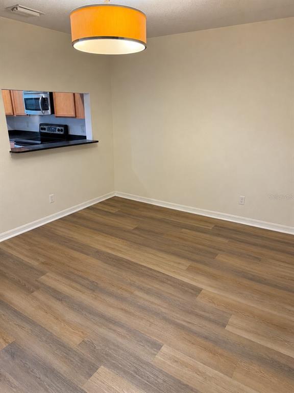 An empty dining area features wood-look flooring, a pass-through window to the kitchen, and a pendant light — 9410 CHARLESBERG DRIVE, TAMPA, FL