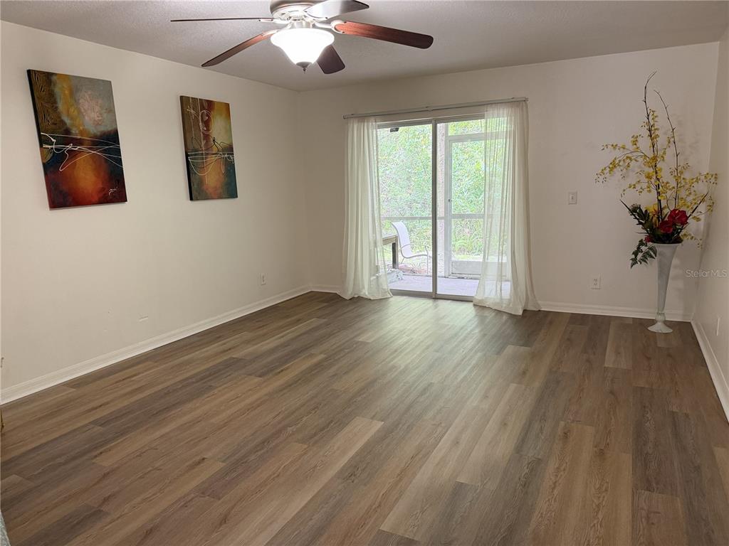 A living room features wood-look flooring, a ceiling fan, wall art, and a sliding glass door — 9410 CHARLESBERG DRIVE, TAMPA, FL