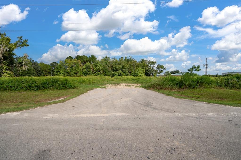 A paved road leads to an overgrown, vacant lot under a bright, cloudy blue sky — 13157 NW 104TH TERRACE, ALACHUA, FL