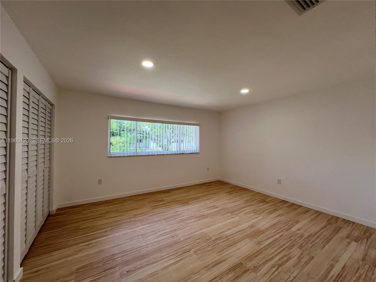 An empty bedroom features light wood-look flooring, white walls, recessed lighting, and louvered closet doors — 8111 SW 81st Pl, Miami FL 33143, MIAMI, FL