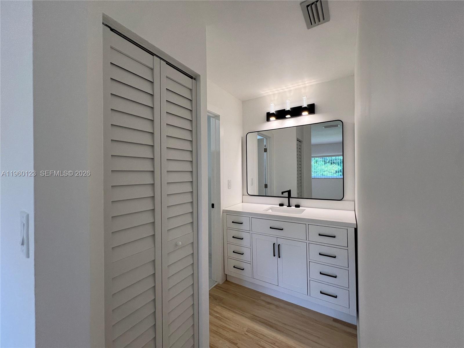A modern bathroom features a white vanity with black hardware, a large mirror, and louvered doors — 8111 SW 81st Pl, Miami FL 33143, MIAMI, FL