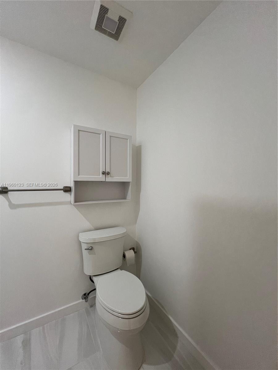 A small bathroom features a white toilet, a wall-mounted cabinet, and a towel bar — 8111 SW 81st Pl, Miami FL 33143, MIAMI, FL
