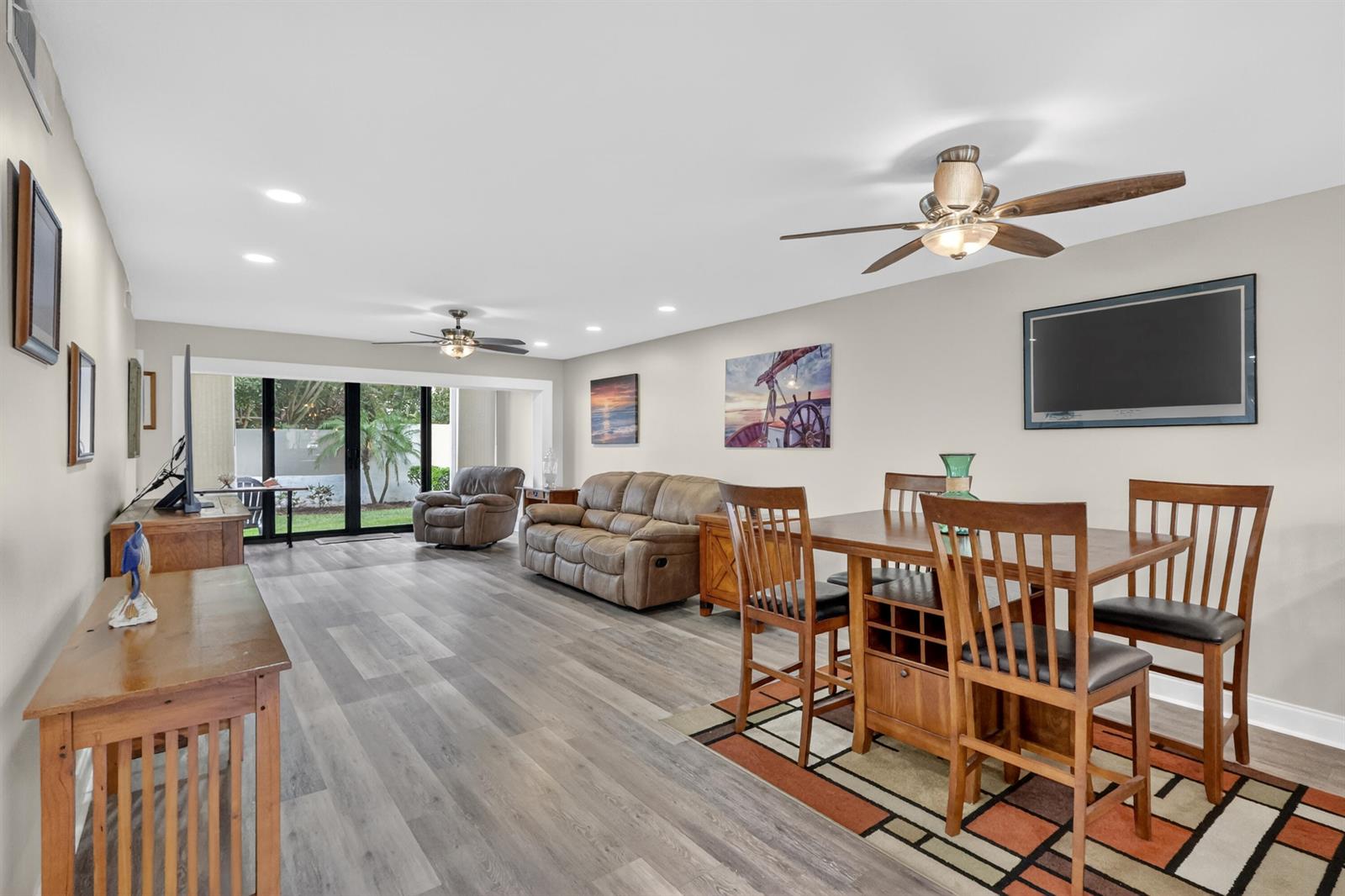 A living and dining area features wood-look flooring, ceiling fans, and a sliding glass door — 1600 NE Dixie Highway # 104, Jensen Beach FL 34957, JENSEN BEACH, FL