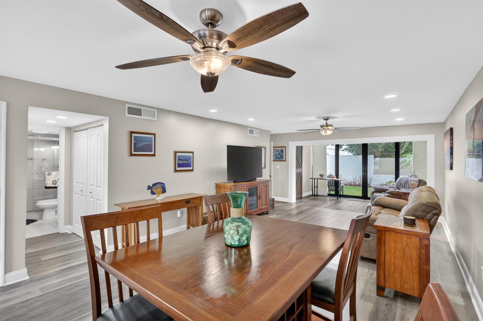 A dining area with a wooden table leads into a living room with sliding doors — 1600 NE Dixie Highway # 104, Jensen Beach FL 34957, JENSEN BEACH, FL