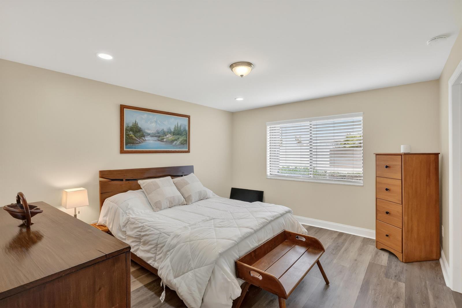 A bedroom features a wooden bed frame, a tall dresser, and a landscape painting — 1600 NE Dixie Highway # 104, Jensen Beach FL 34957, JENSEN BEACH, FL