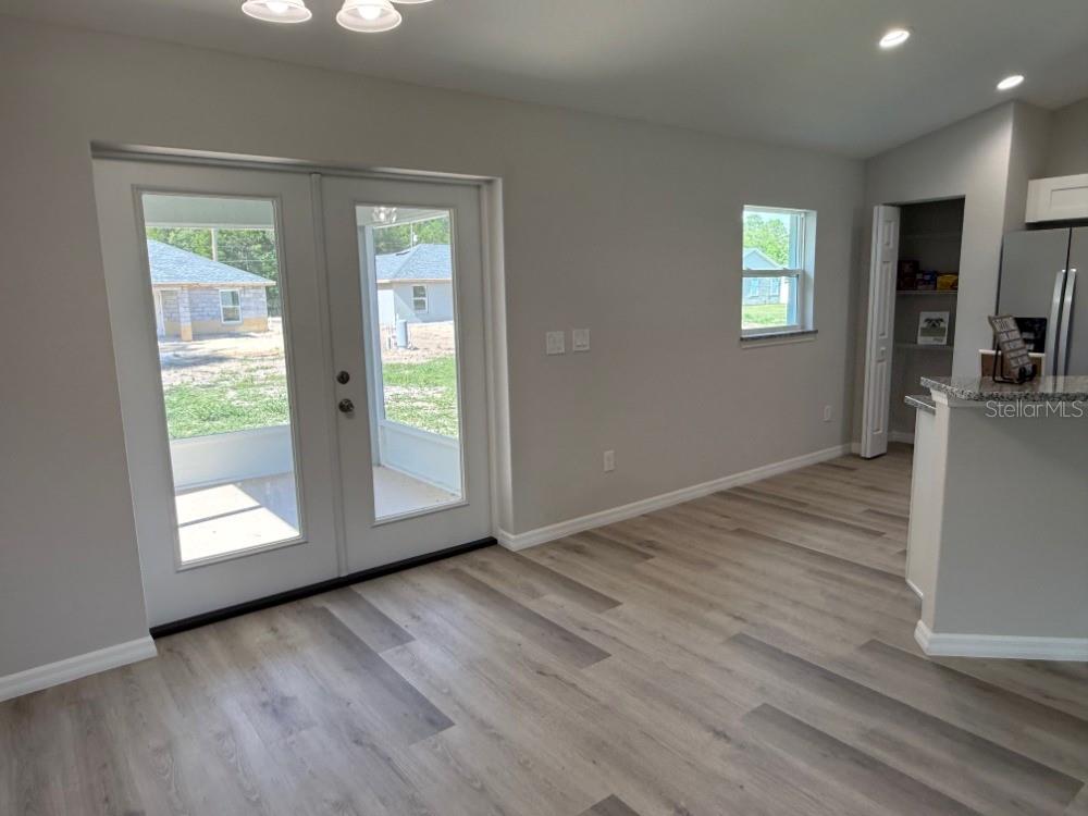 A dining area with light wood-look flooring, double glass doors, and an adjacent kitchen pantry — 13330 SW 111 LANE, DUNNELLON, FL