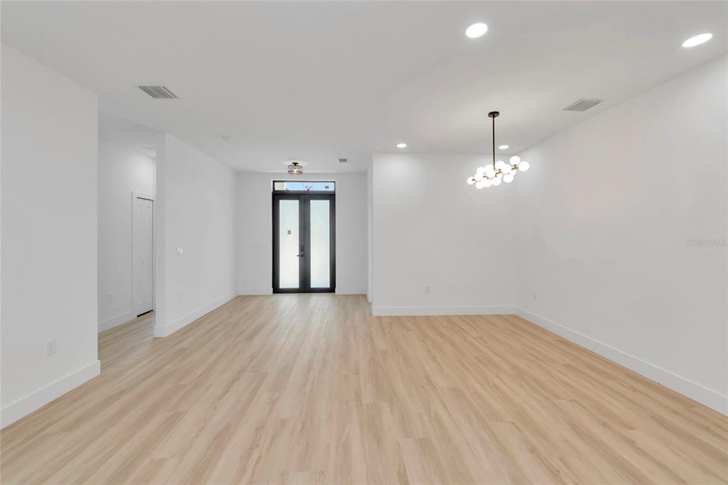 An empty room features light wood-look flooring, white walls, recessed lighting, and a modern globe chandelier — 1274 RONALD STREET, NORTH PORT, FL