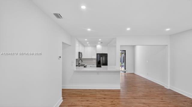 A kitchen with white cabinets and a breakfast bar opens into a living area — 1010 NE 138th St, North Miami FL 33161, NORTH MIAMI, FL