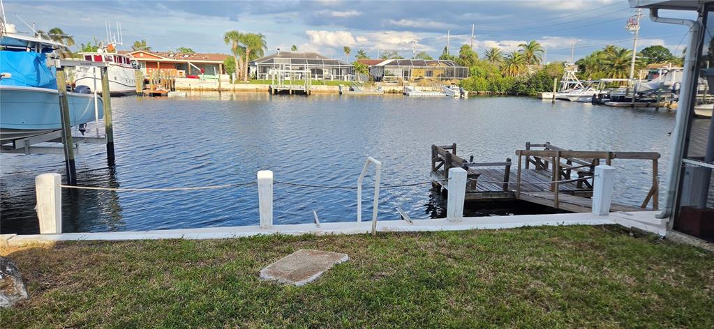 A waterfront view from a grassy backyard featuring a wooden dock and boat lift — 5308 PILOTS PLACE, NEW PORT RICHEY, FL