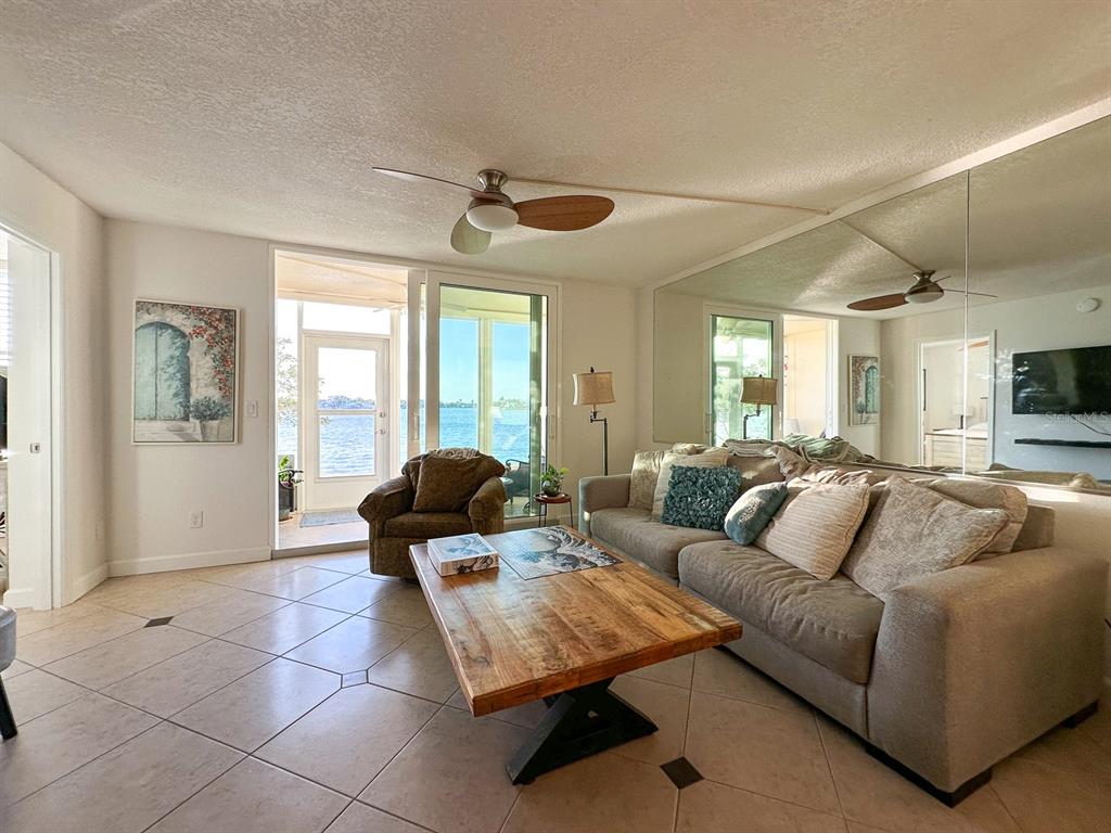 A living room features tile floors, a wooden coffee table, and a view of water — 7920 SUN ISLAND DRIVE S UNIT 102, SOUTH PASADENA, FL
