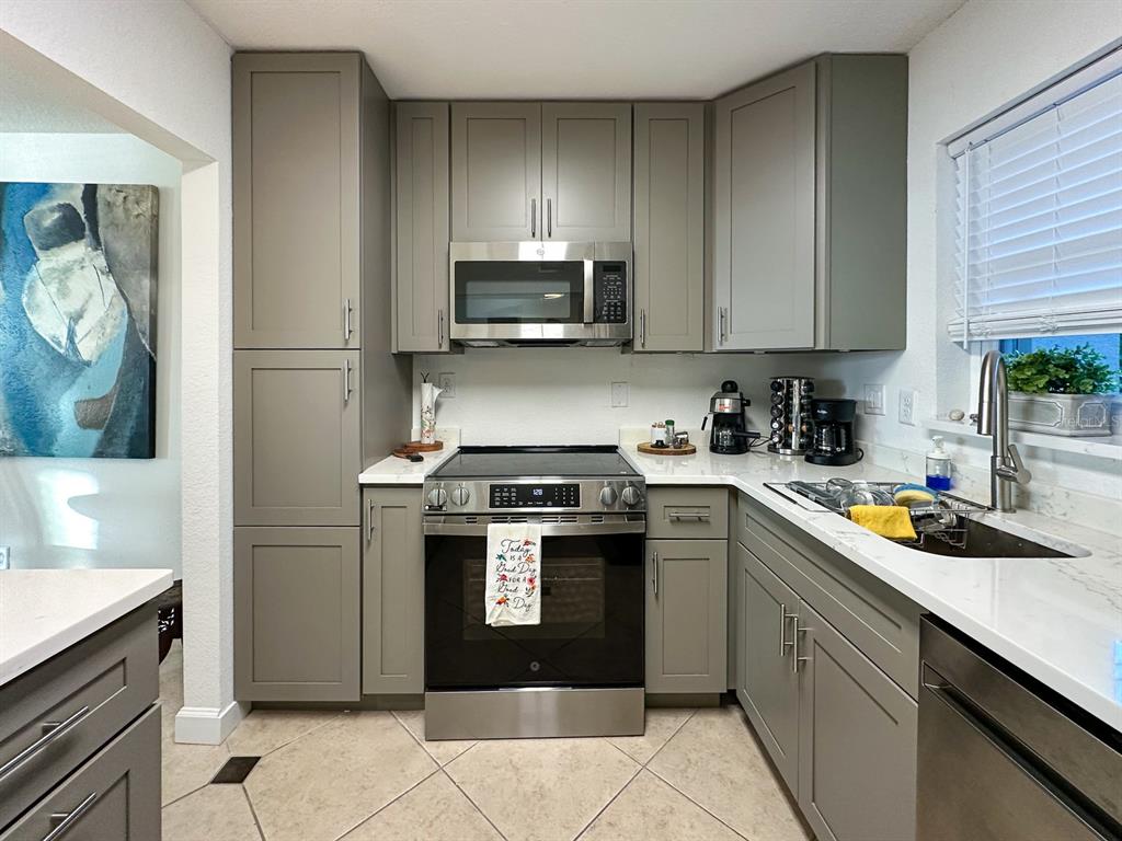 A kitchen features gray shaker cabinets, stainless steel appliances, and white quartz countertops — 7920 SUN ISLAND DRIVE S UNIT 102, SOUTH PASADENA, FL