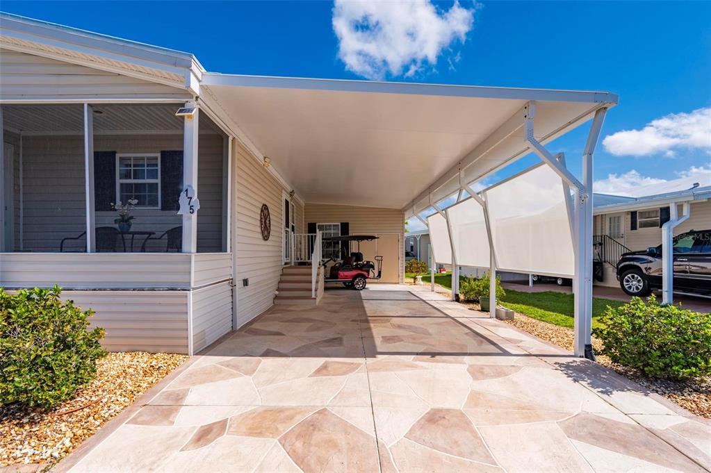 A mobile home exterior features a covered carport with a decorative stone-patterned concrete driveway — 1000 KINGS HIGHWAY UNIT 175, PORT CHARLOTTE, FL