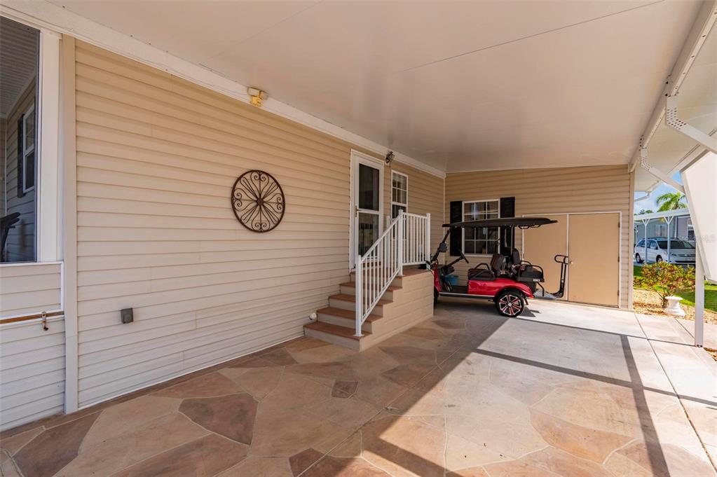 A covered patio with stone-patterned flooring, stairs to a doorway, and a parked golf cart — 1000 KINGS HIGHWAY UNIT 175, PORT CHARLOTTE, FL