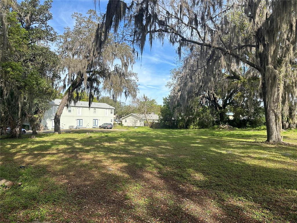 A grassy, tree-shaded vacant lot sits in front of a two-story residential building — EUCLID AVENUE, LEESBURG, FL