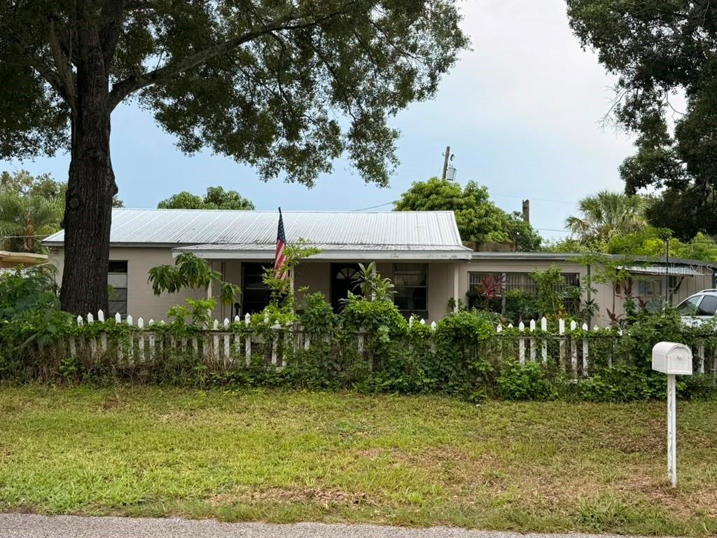 A single-story house with a metal roof and a white picket fence behind a lawn — 4203 S TRASK STREET, TAMPA, FL