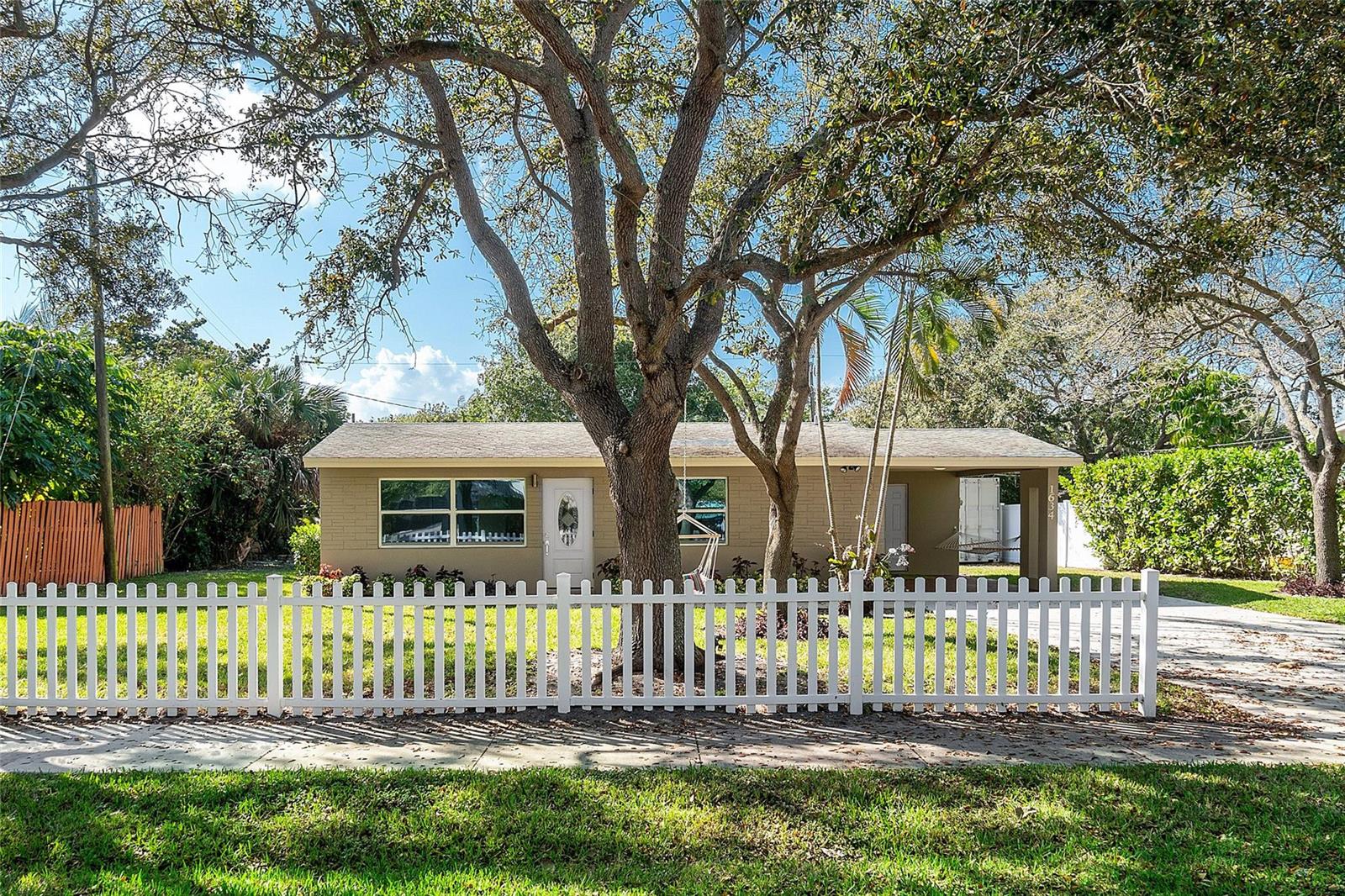 A single-story tan house with a white picket fence and a large tree in front — 1634 NE 3rd Avenue, Delray Beach FL 33444, DELRAY BEACH, FL
