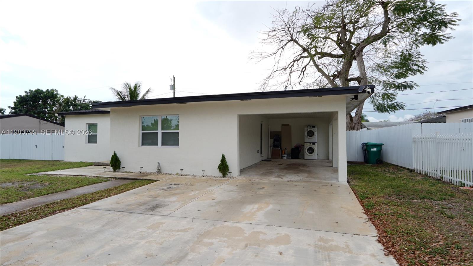 A white single-story house features a concrete driveway, a carport, and a stacked laundry unit — 14580 Harrison St, Miami FL 33176, MIAMI, FL