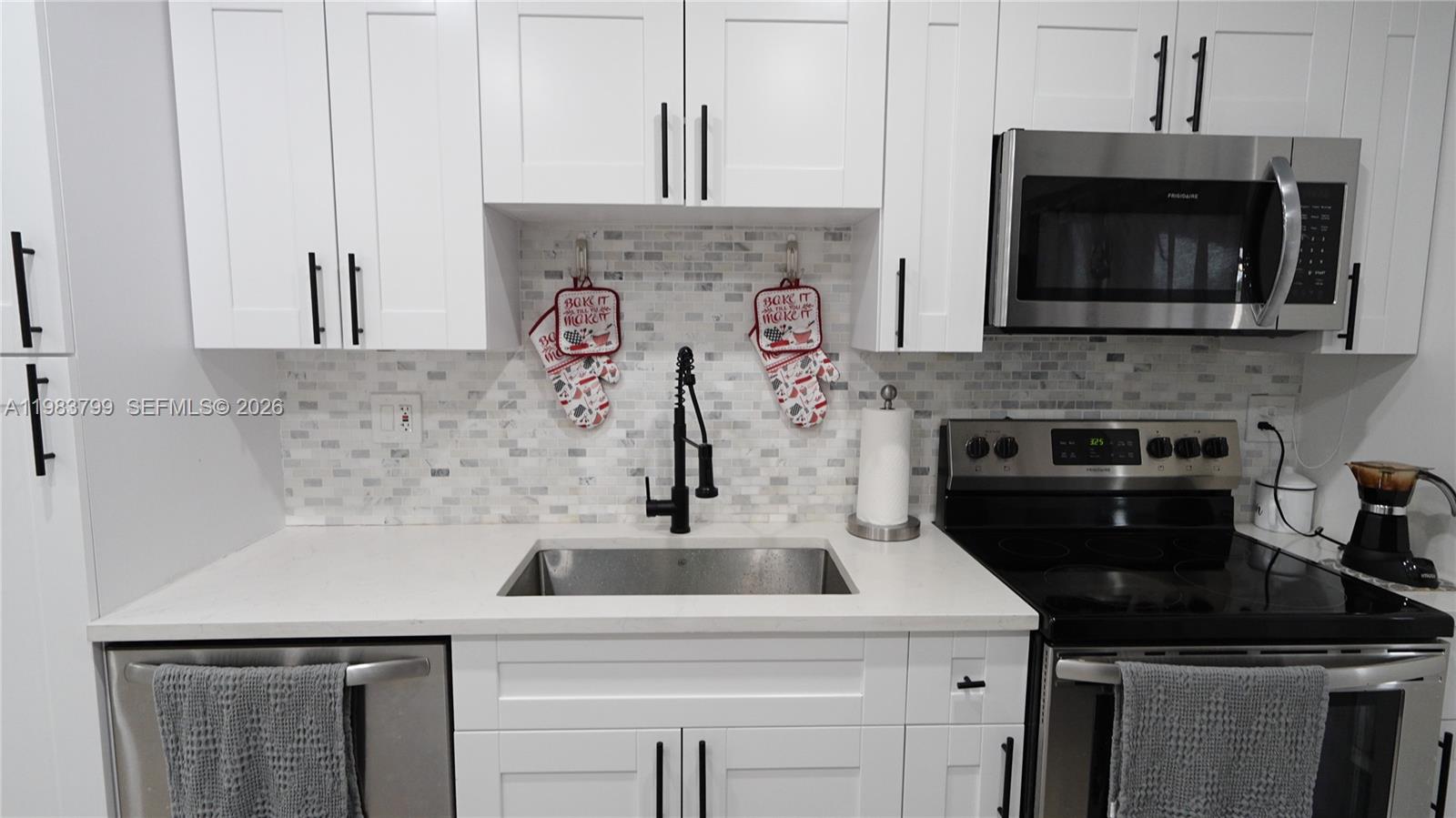 A kitchen features white cabinets, a stainless steel sink, a black faucet, and a tiled backsplash — 14580 Harrison St, Miami FL 33176, MIAMI, FL