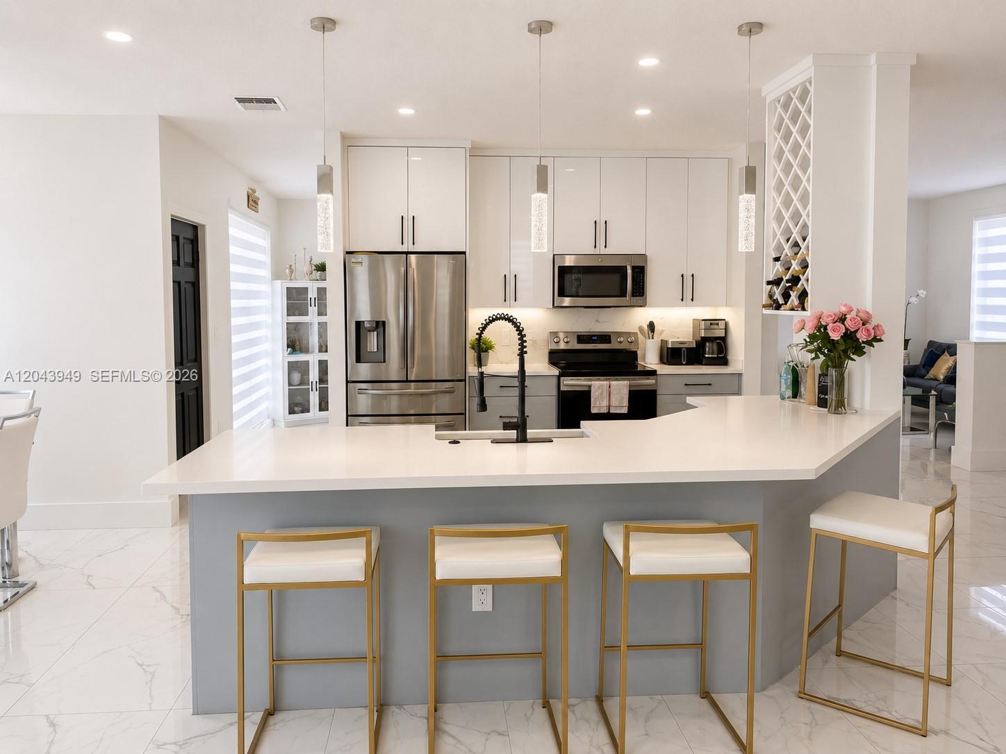 A modern kitchen features white cabinets, stainless steel appliances, a gray island, and gold barstools — 2855 SW 177th Ter, Miramar FL 33029, MIRAMAR, FL