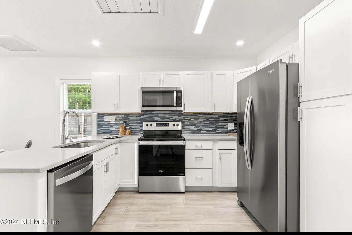 A modern kitchen features white cabinets, stainless steel appliances, and a blue tiled backsplash — 925 S St. John Street, FL 32084, FL