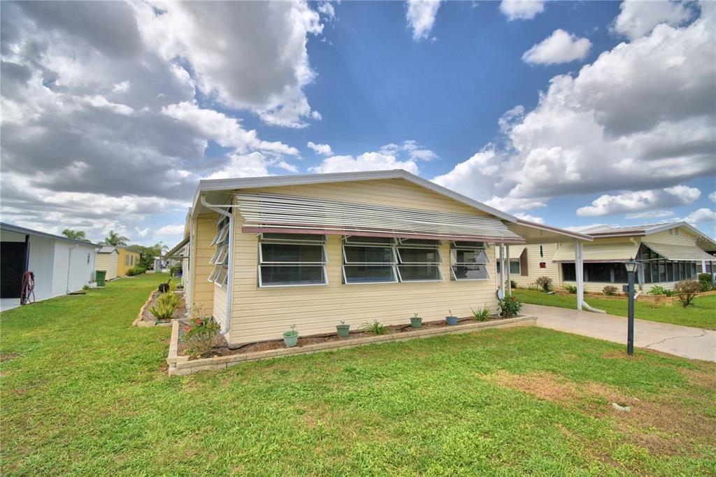 A light yellow mobile home with a metal awning over its front windows and carport — 6773 BRENTWOOD DRIVE NE, WINTER HAVEN, FL
