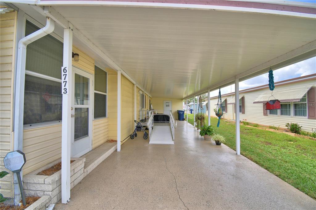 A covered carport area features a concrete floor, a wheelchair ramp, and yellow exterior siding — 6773 BRENTWOOD DRIVE NE, WINTER HAVEN, FL
